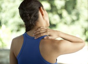 Junge Frau in Sportbekleidung hält sich mit der Hand den Nacken.